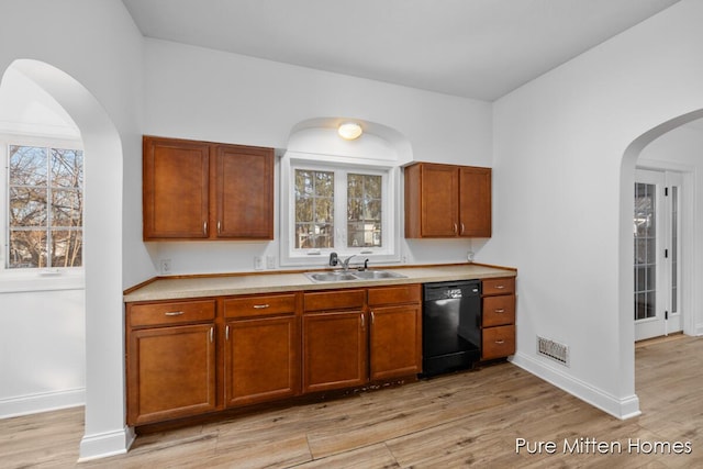 kitchen with light wood-type flooring, black dishwasher, visible vents, and a sink