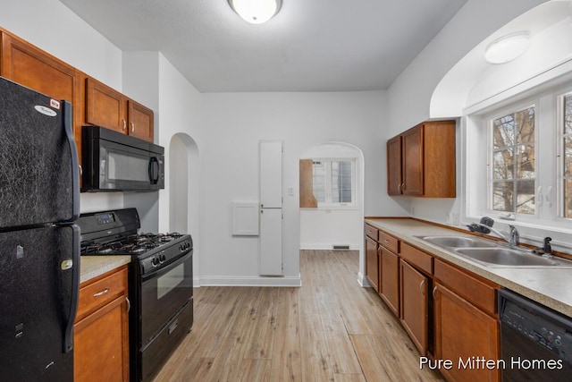 kitchen featuring arched walkways, light countertops, a sink, light wood-type flooring, and black appliances