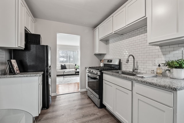 kitchen featuring light wood-style flooring, a sink, white cabinetry, freestanding refrigerator, and stainless steel range with gas stovetop