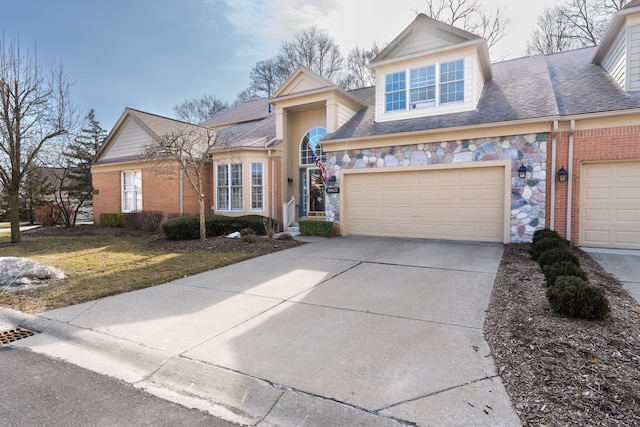 view of front facade featuring stone siding, roof with shingles, brick siding, and concrete driveway