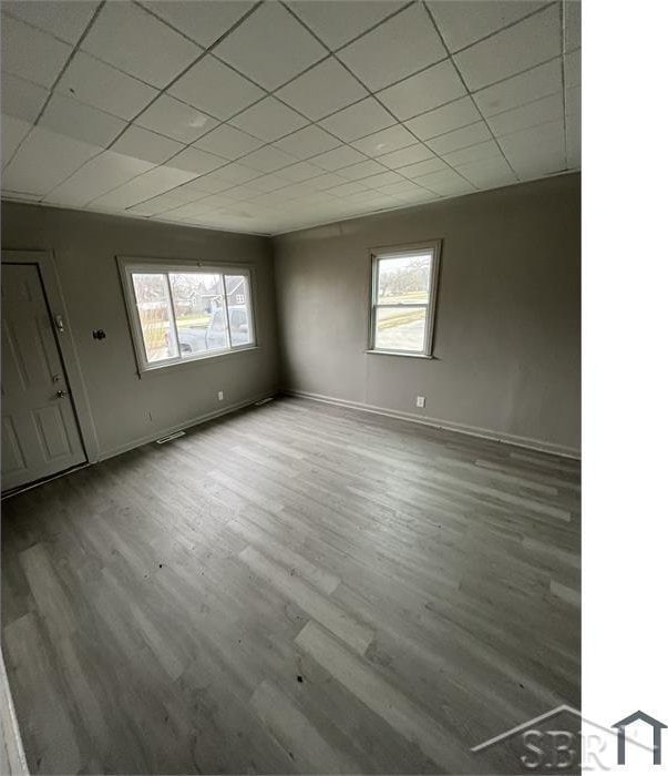 unfurnished room with baseboards, a healthy amount of sunlight, a drop ceiling, and wood finished floors