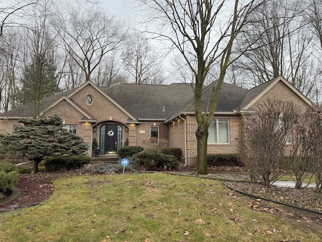 ranch-style home featuring a shingled roof, a front yard, and brick siding