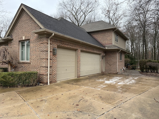 view of home's exterior featuring brick siding, driveway, an attached garage, and roof with shingles