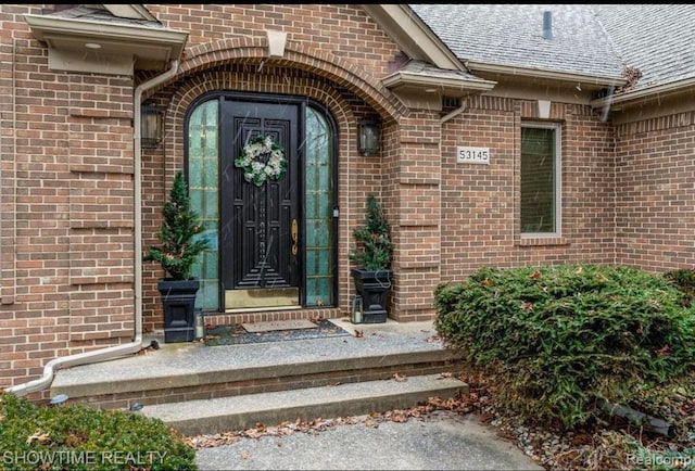 doorway to property with a shingled roof and brick siding