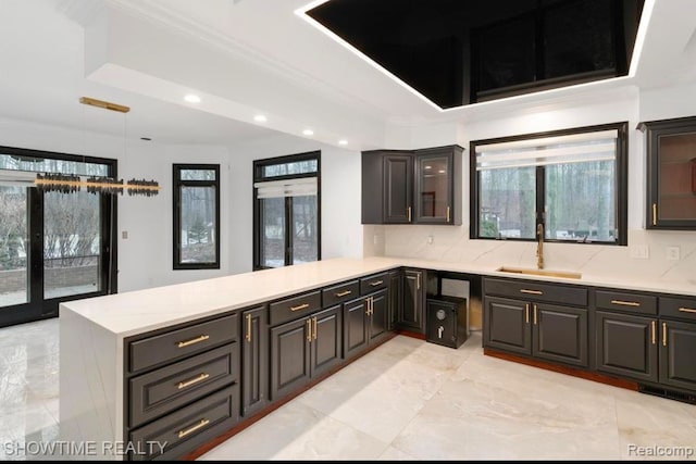 kitchen featuring glass insert cabinets, a peninsula, marble finish floor, pendant lighting, and a sink