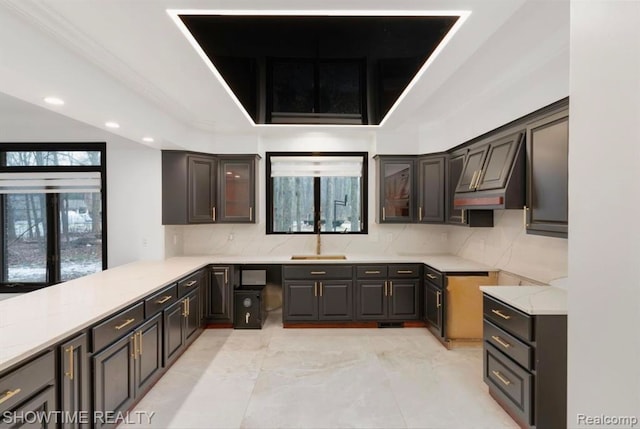 kitchen with a peninsula, glass insert cabinets, decorative backsplash, and a sink