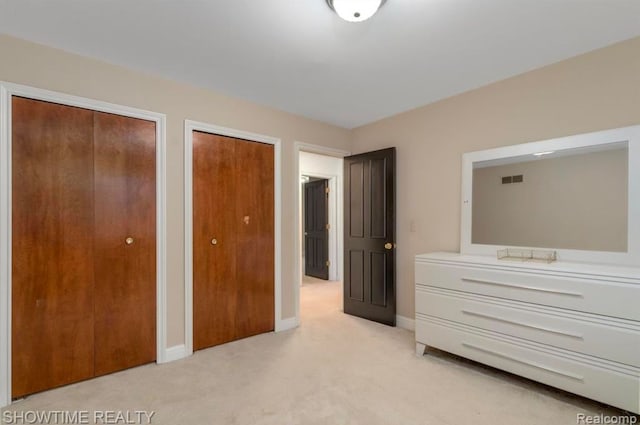 unfurnished bedroom featuring multiple closets, light colored carpet, visible vents, and baseboards