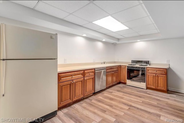 kitchen with brown cabinets, stainless steel dishwasher, freestanding refrigerator, gas stove, and light wood-type flooring