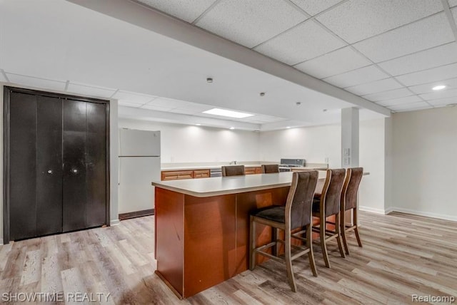 kitchen featuring baseboards, a drop ceiling, freestanding refrigerator, light countertops, and light wood-style floors