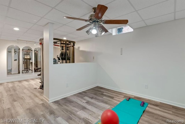 exercise room with wood finished floors, a paneled ceiling, and baseboards