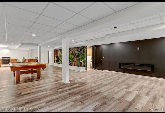 rec room featuring a glass covered fireplace, a drop ceiling, baseboards, and wood finished floors