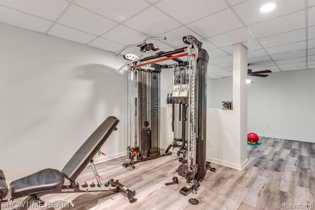 exercise area featuring a ceiling fan, a paneled ceiling, baseboards, and wood finished floors