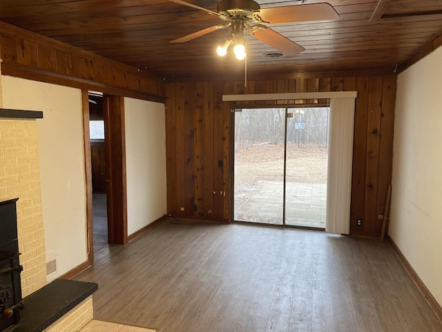 unfurnished living room featuring visible vents, wooden walls, wood finished floors, wooden ceiling, and baseboards