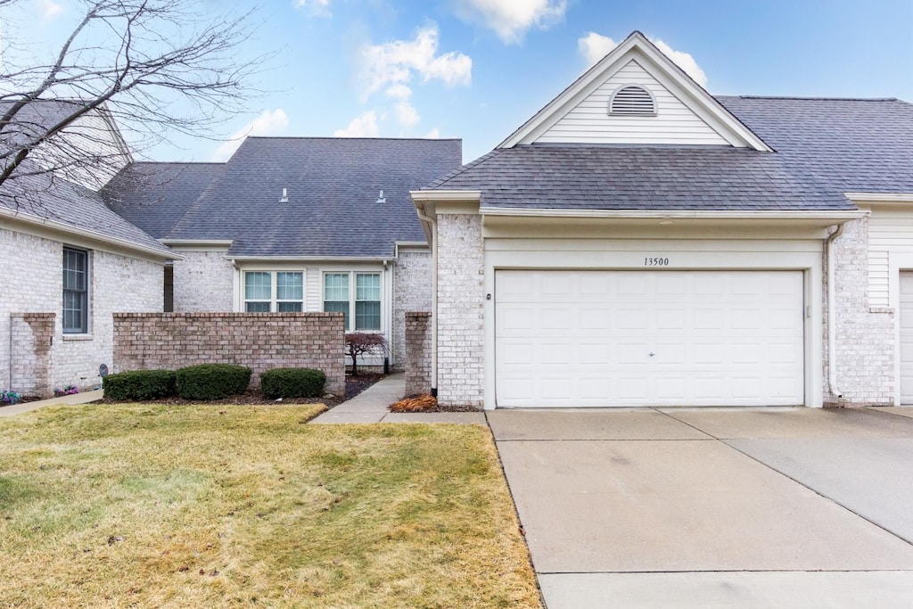 view of front facade featuring brick siding, a shingled roof, concrete driveway, an attached garage, and a front lawn