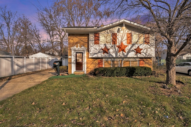 view of front facade featuring brick siding, fence, and a yard