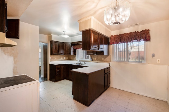 kitchen with dark brown cabinetry, a peninsula, an inviting chandelier, light countertops, and a sink