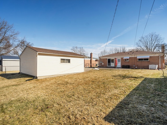 back of house featuring an outbuilding, brick siding, a lawn, and fence