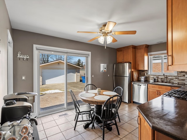 kitchen featuring a sink, appliances with stainless steel finishes, backsplash, brown cabinetry, and dark countertops