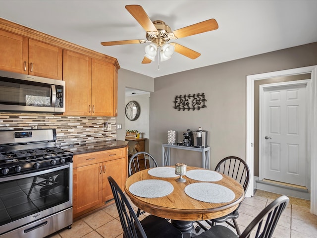 kitchen with light tile patterned floors, appliances with stainless steel finishes, brown cabinets, tasteful backsplash, and dark countertops