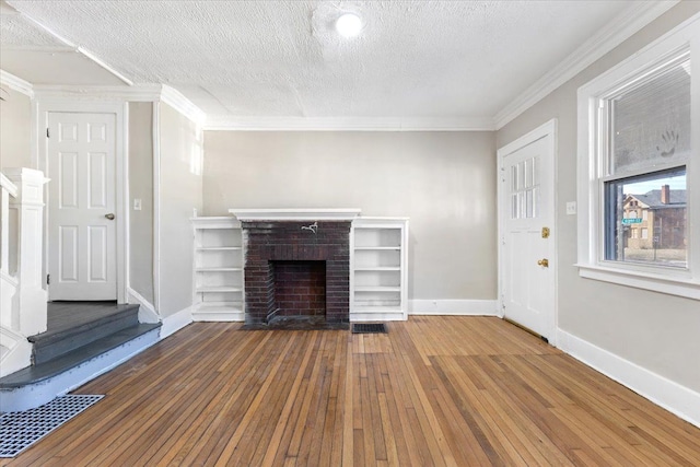 unfurnished living room with baseboards, hardwood / wood-style floors, crown molding, a textured ceiling, and a brick fireplace