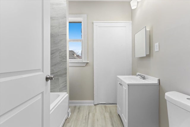 bathroom with baseboards, toilet, a bathing tub, wood finished floors, and vanity