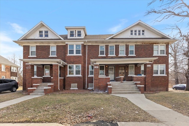 view of property with a porch, a front yard, and brick siding