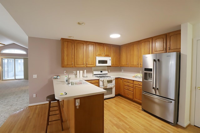 kitchen featuring a peninsula, white appliances, brown cabinetry, and a sink