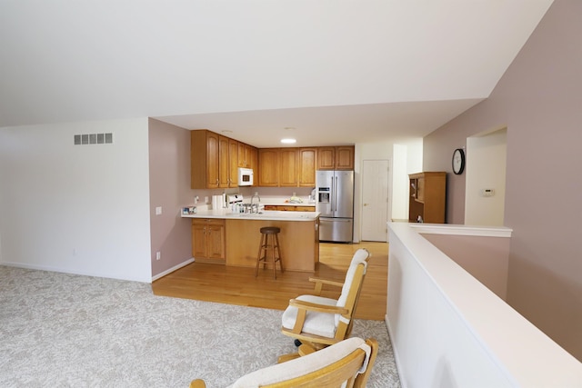 kitchen with stainless steel refrigerator with ice dispenser, light countertops, visible vents, white microwave, and a peninsula