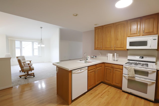 kitchen featuring light countertops, a sink, light wood-type flooring, white appliances, and a peninsula