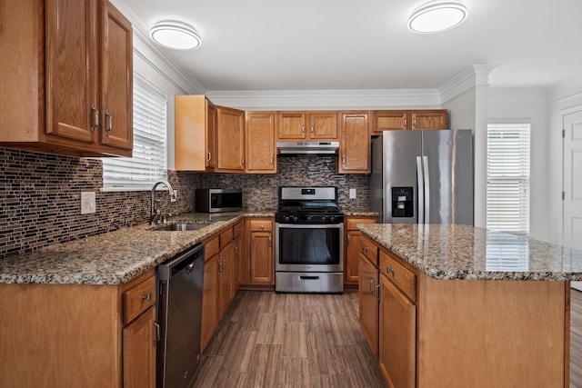 kitchen featuring crown molding, stainless steel appliances, brown cabinetry, a sink, and under cabinet range hood