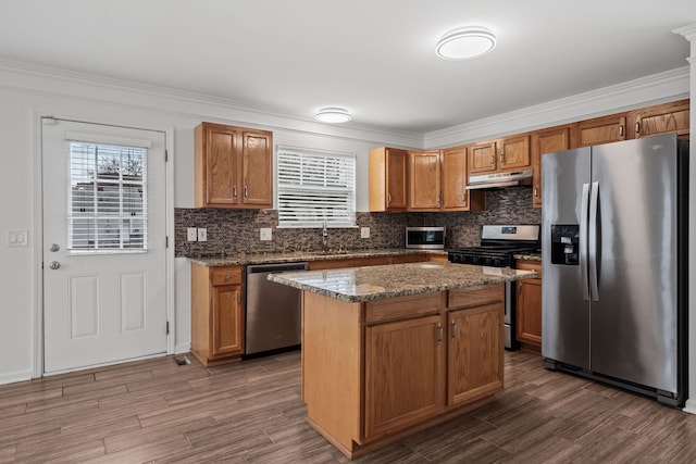 kitchen with dark wood-style floors, appliances with stainless steel finishes, stone counters, and under cabinet range hood