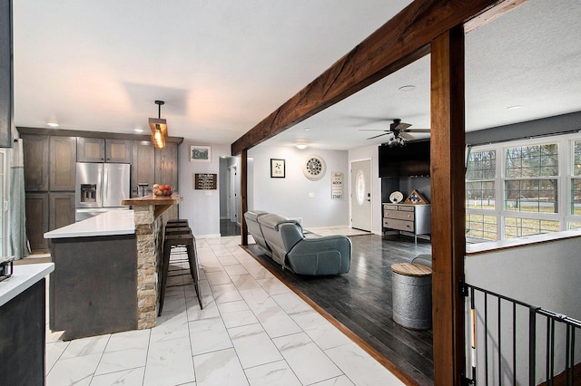 kitchen featuring beamed ceiling, marble finish floor, light countertops, a kitchen bar, and stainless steel refrigerator with ice dispenser