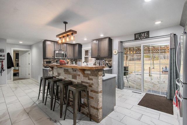 kitchen with decorative backsplash, appliances with stainless steel finishes, hanging light fixtures, marble finish floor, and a kitchen bar