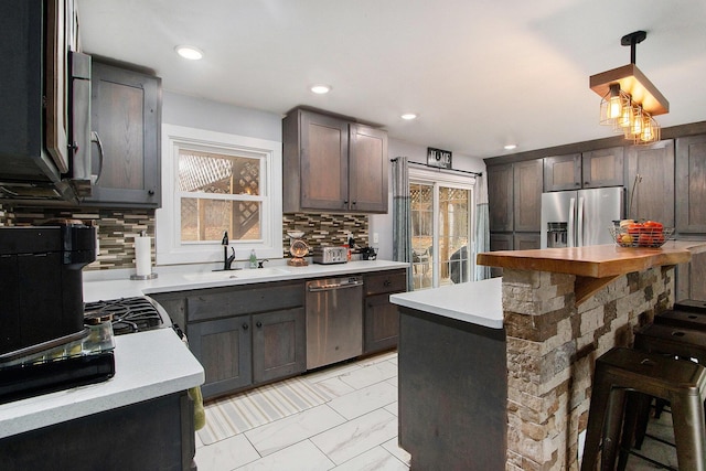 kitchen featuring a sink, marble finish floor, light countertops, appliances with stainless steel finishes, and decorative backsplash