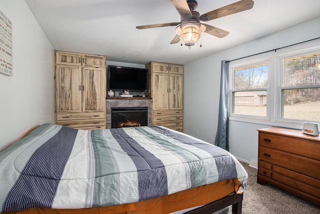 carpeted bedroom with ceiling fan, a lit fireplace, and baseboards