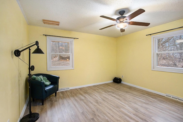 living area with a wealth of natural light, visible vents, a textured ceiling, and wood finished floors