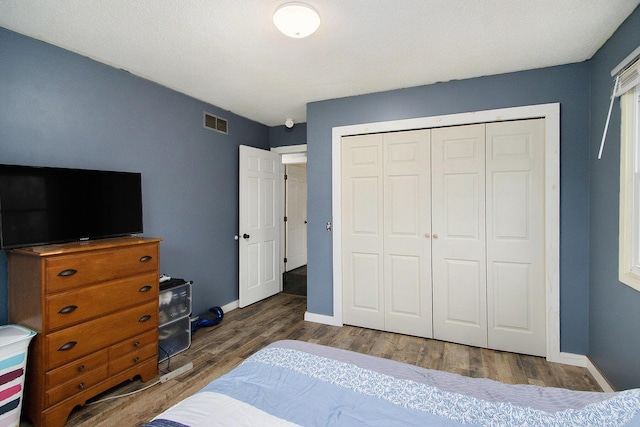 bedroom with a closet, visible vents, baseboards, and wood finished floors