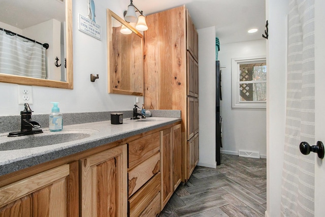 full bath featuring double vanity, a sink, visible vents, and baseboards