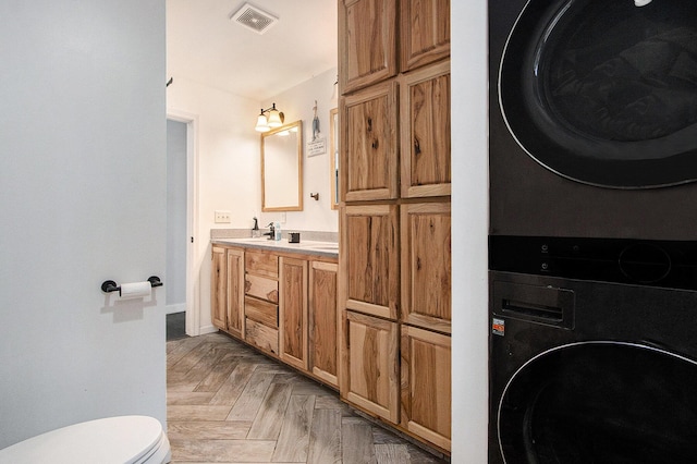 bathroom featuring visible vents, toilet, vanity, stacked washing maching and dryer, and baseboards