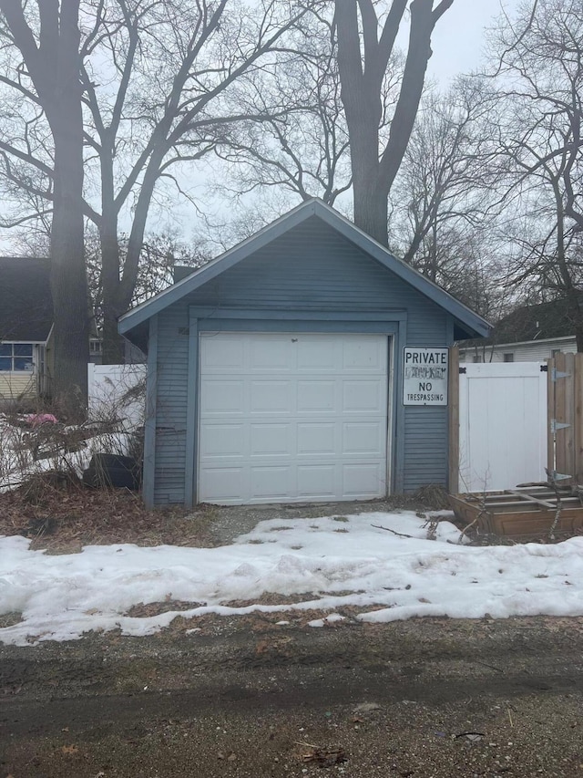 snow covered garage featuring a detached garage and fence