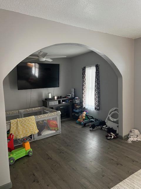 interior space featuring arched walkways, a textured ceiling, wood finished floors, and a ceiling fan