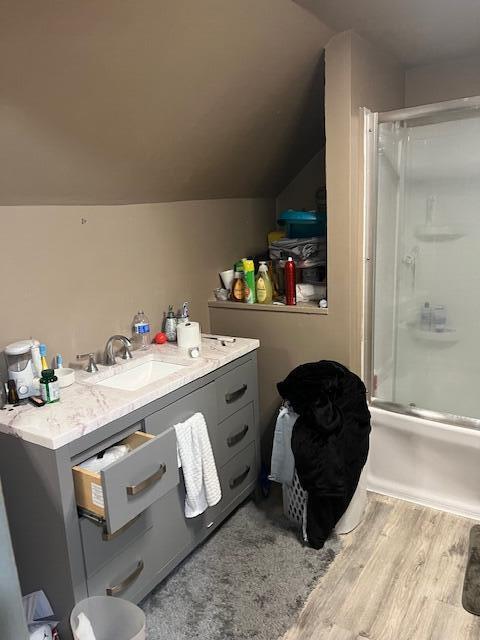 bathroom with shower / bath combination with glass door, vaulted ceiling, wood finished floors, and vanity