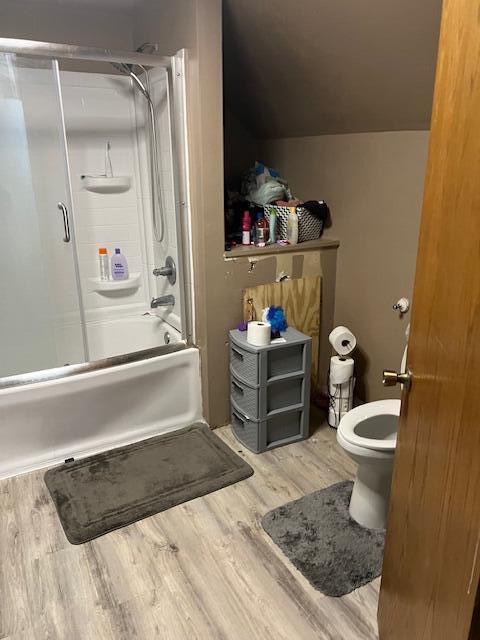 bathroom with toilet, bath / shower combo with glass door, and wood finished floors