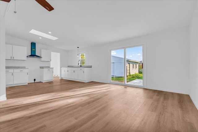 unfurnished living room with a skylight, baseboards, light wood finished floors, and recessed lighting