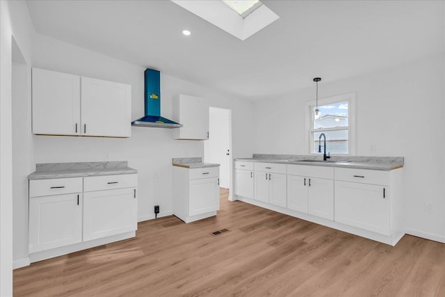 kitchen featuring visible vents, white cabinetry, a sink, and wall chimney range hood