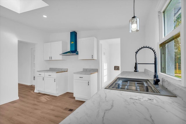 kitchen featuring wall chimney exhaust hood, light stone counters, white cabinets, and a sink