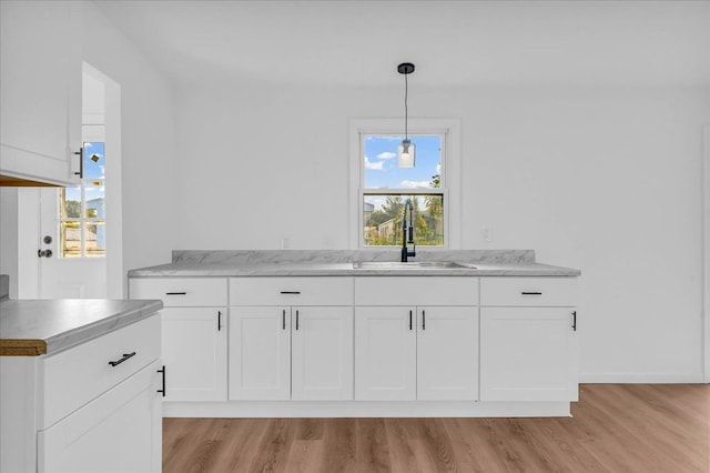 kitchen with light wood-style floors, white cabinets, a sink, and decorative light fixtures