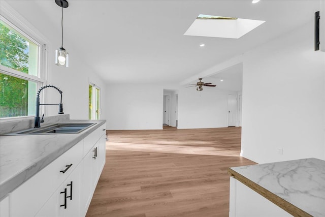 kitchen featuring a skylight, hanging light fixtures, light wood-style floors, white cabinetry, and a sink