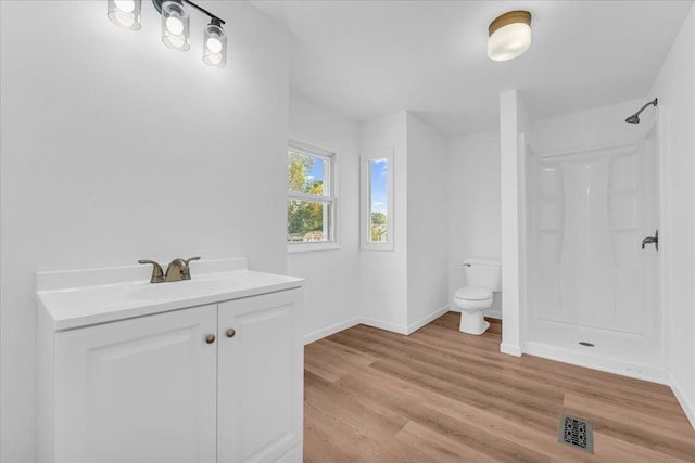 bathroom featuring toilet, wood finished floors, vanity, visible vents, and a shower