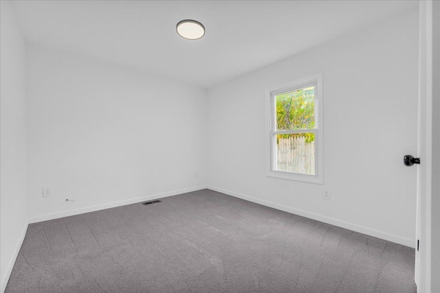 empty room featuring baseboards, visible vents, and dark carpet